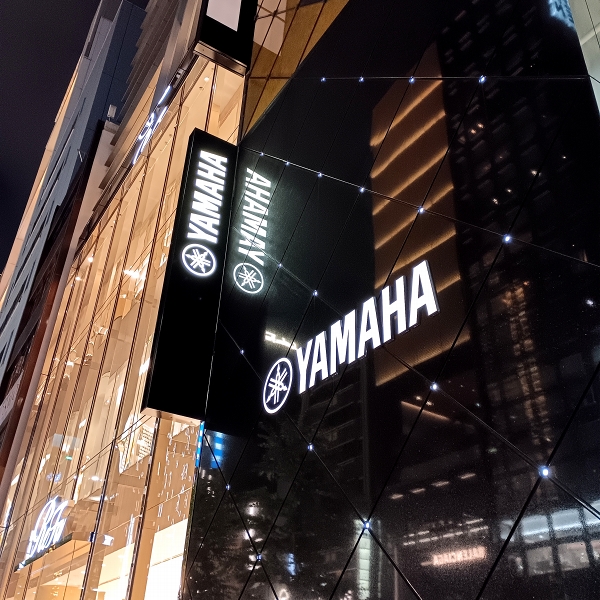 夜の銀座にあるヤマハ銀座店の外観/ライトアップされた建物のガラスファサードが街の光を反射している